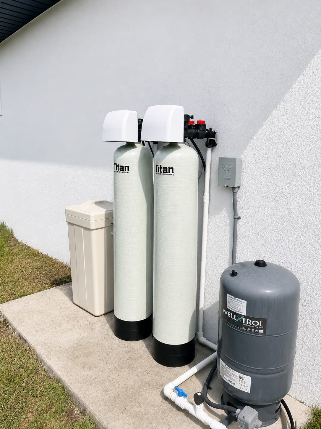 A Titan two-tank well water system and salt tank installed against a stucco wall